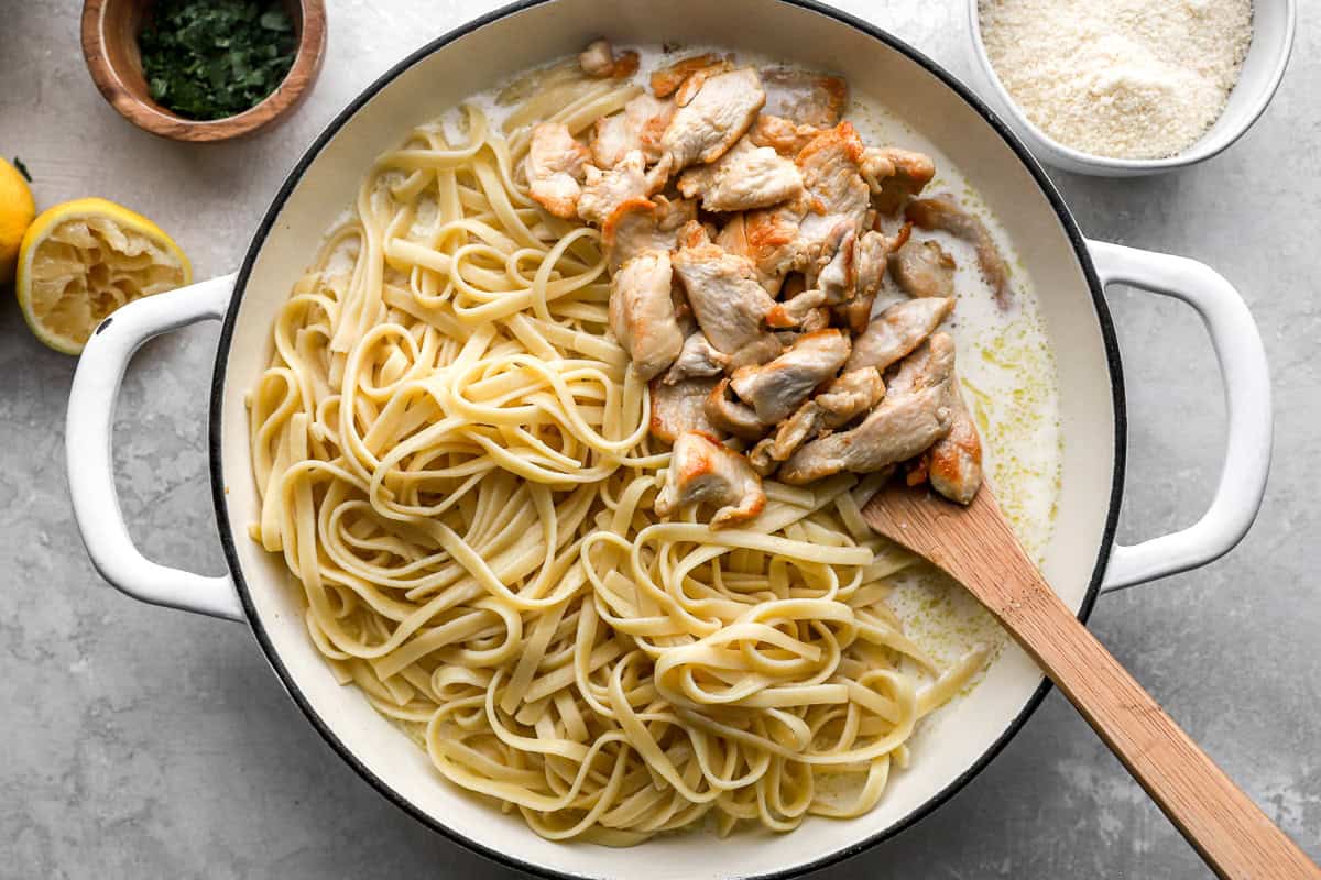 cooked chicken slices and pasta in a pan with alfredo sauce.