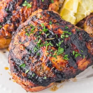 closeup of grilled chicken thigh on a white plate.