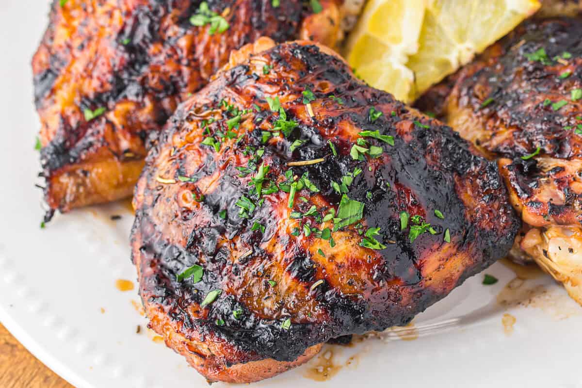 closeup of grilled chicken thigh on a white plate.