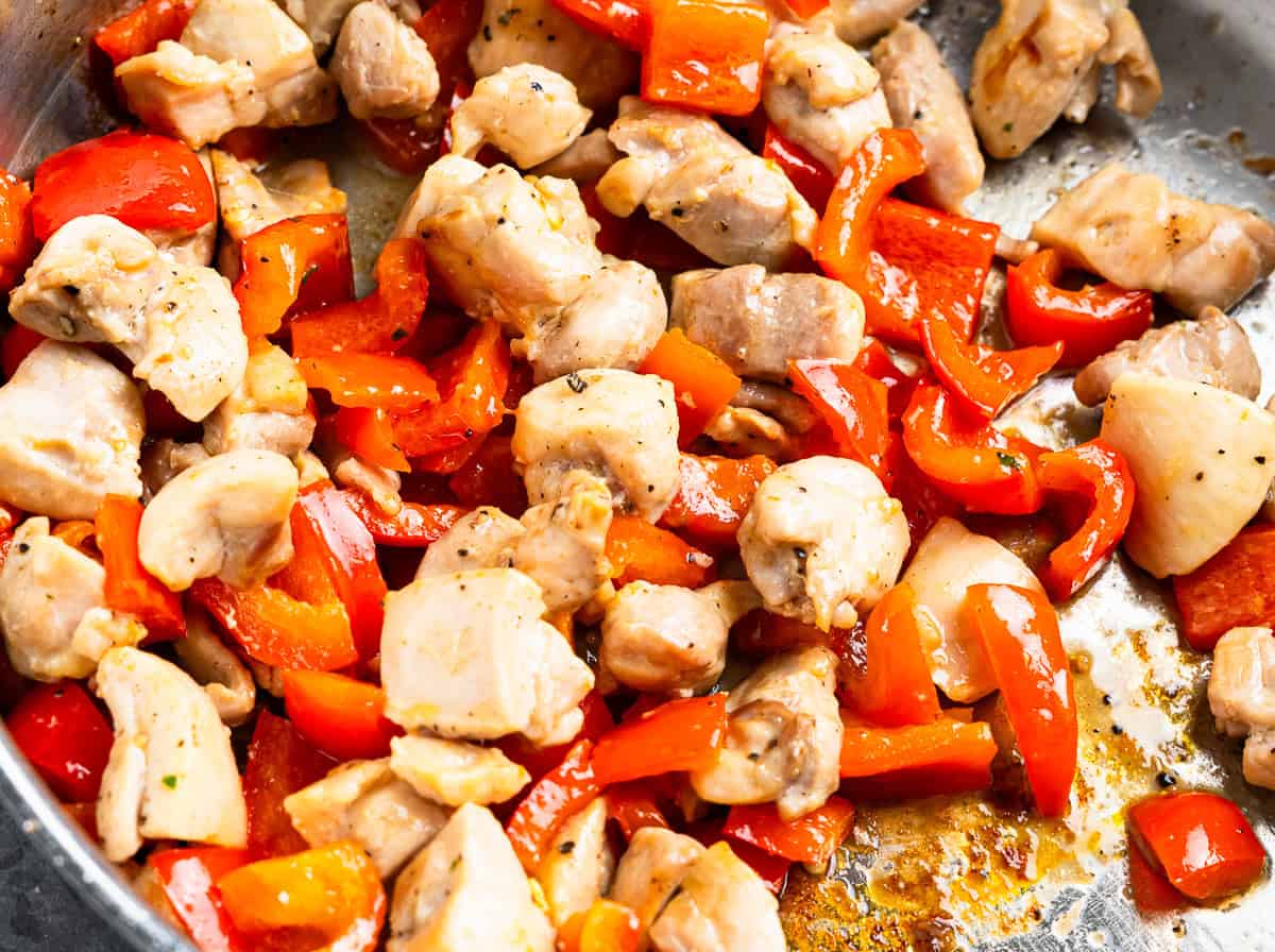 chicken and red pepper chunks cooking in a pan.