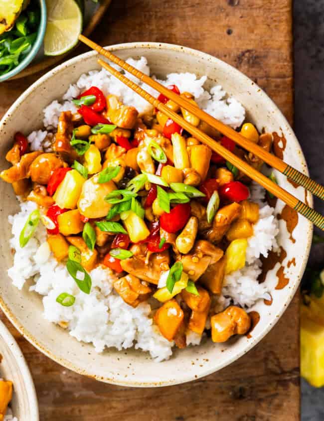 overhead view of a bowl of pineapple chicken over rice with chopsticks.