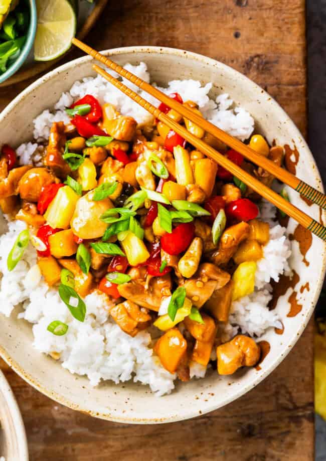 overhead view of a bowl of pineapple chicken over rice with chopsticks.