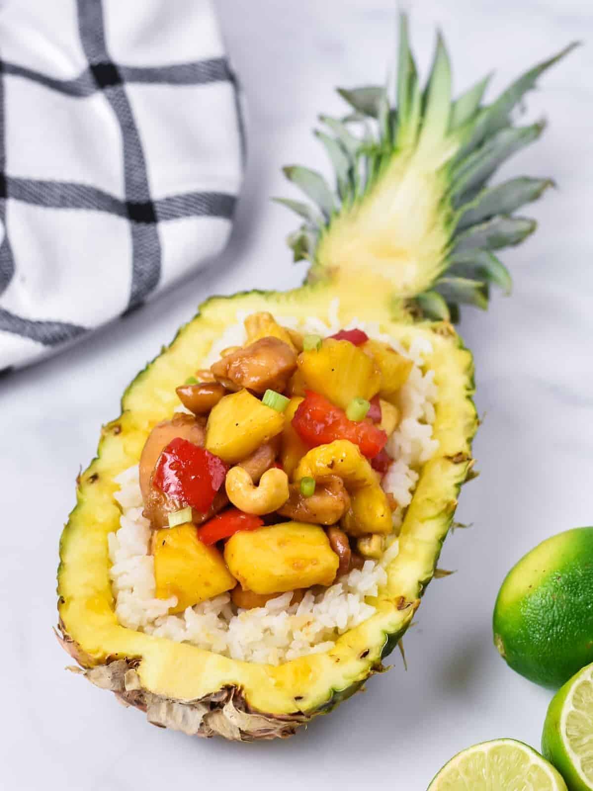 pineapple chicken served on a bed of white rice inside of half a pineapple