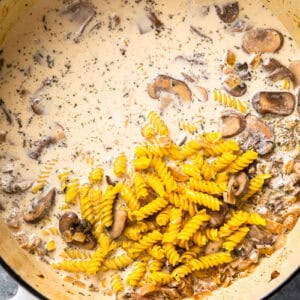 pasta and cream added to sautéed mushrooms in a dutch oven.