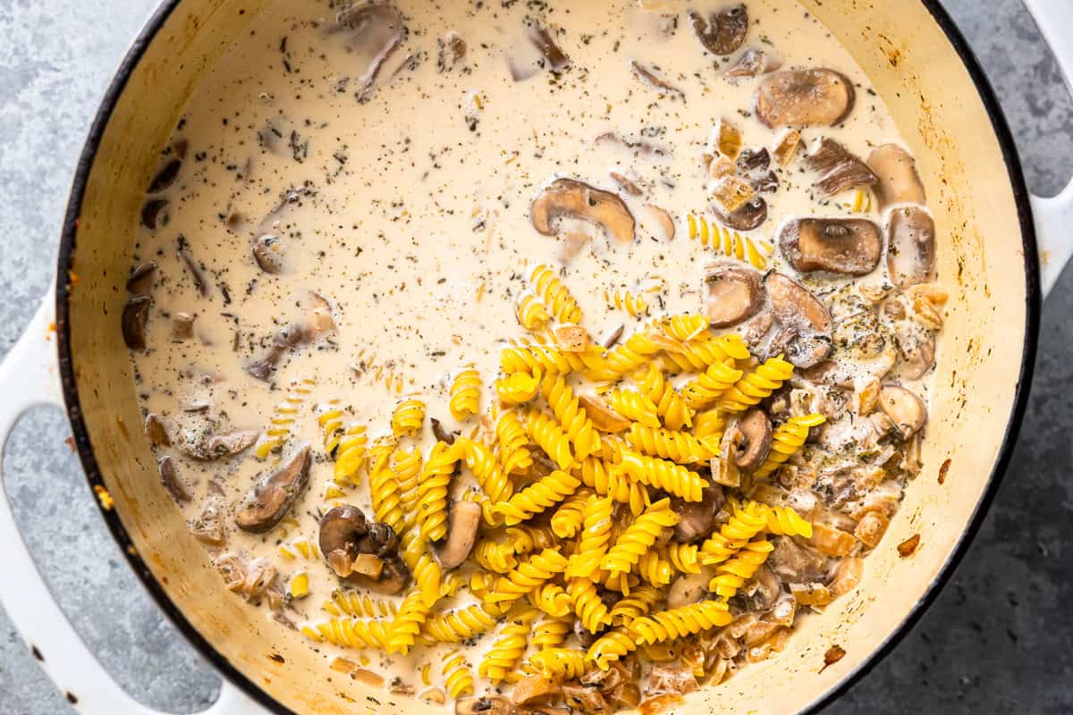pasta and cream added to sautéed mushrooms in a dutch oven.