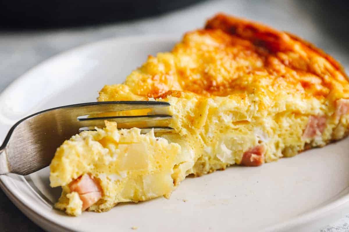 cutting into a slice of ham and cheese frittata with a fork.