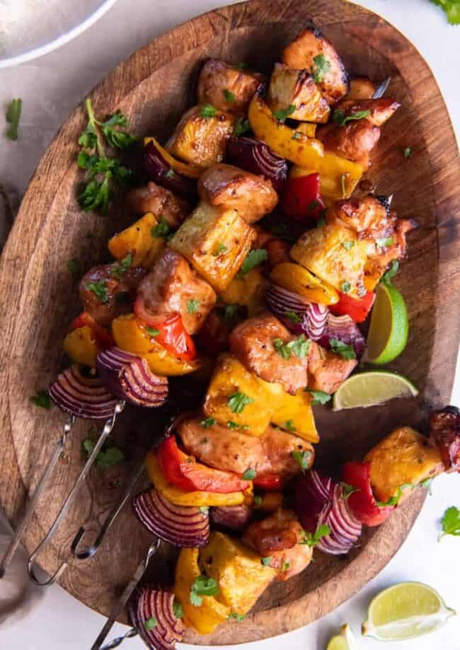 4 hawaiian chicken kabobs on a wooden serving tray.