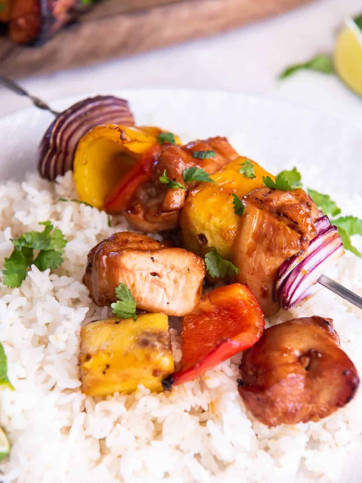 hawaiian chicken kabobs on a bed of white rice on a white plate.
