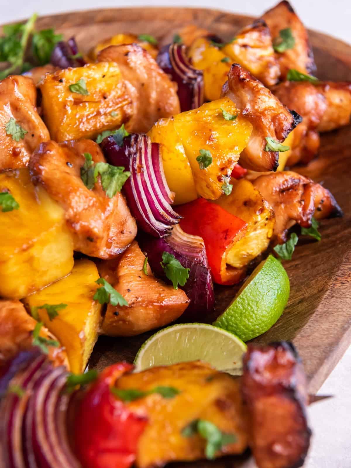 close up of hawaiian chicken kabobs on a wooden serving tray.