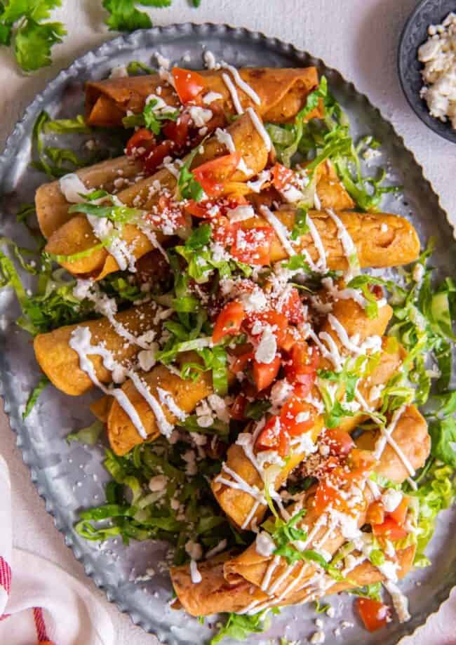 overhead view of a platter of chicken taquitos, garnished with tomatoes, lettuce, and more
