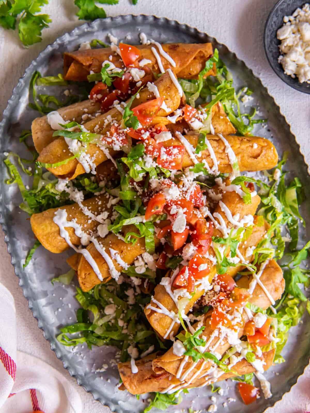 overhead view of a platter of chicken taquitos, garnished with tomatoes, lettuce, and more