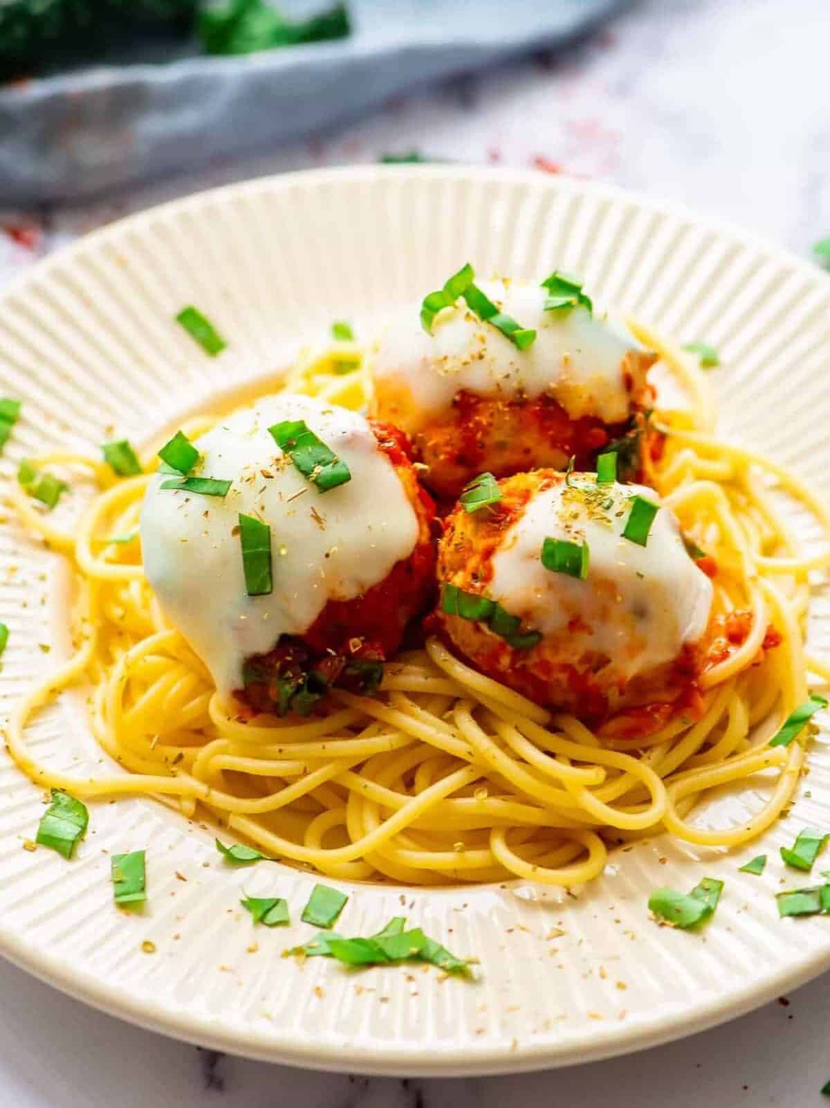 three cheesy Italian chicken meatballs on a plate over pasta