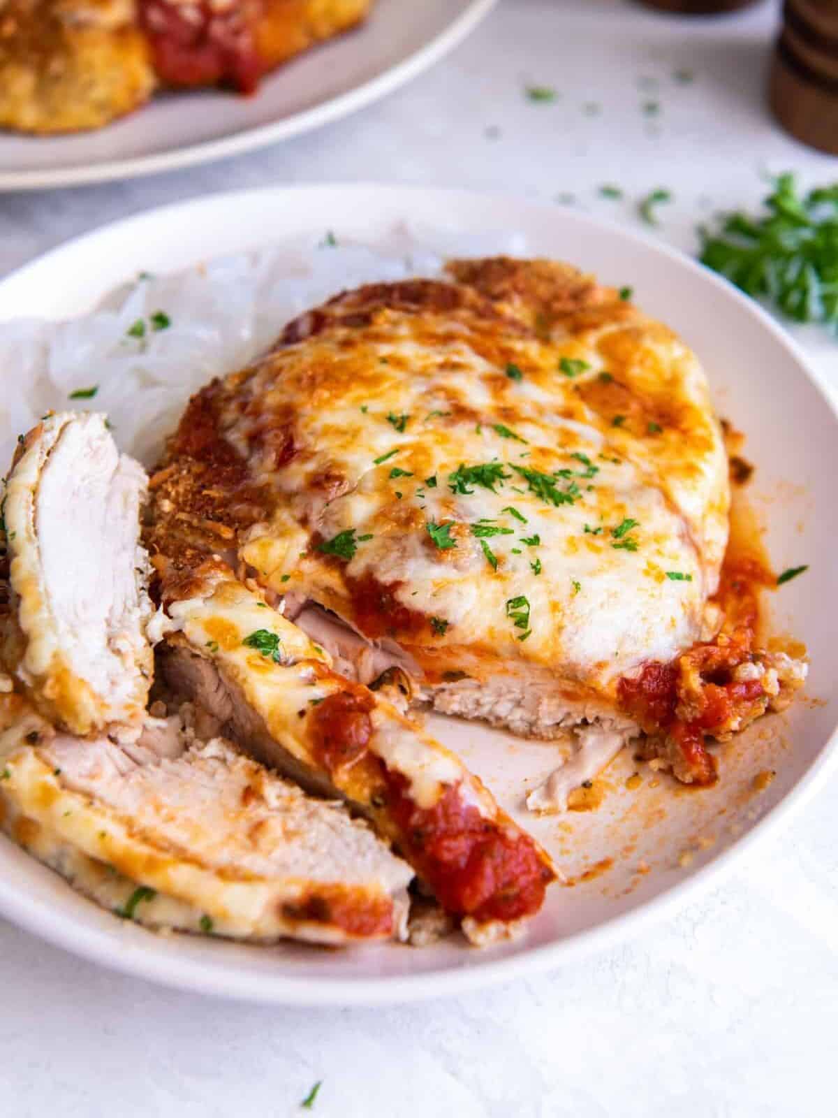 partially sliced keto chicken parmesan on a white plate.