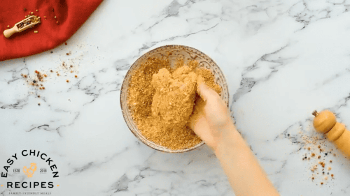 dipping a chicken thigh in seasoned breadcrumbs.