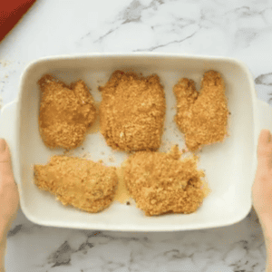 breaded chicken thighs in a baking dish topped with melted butter.