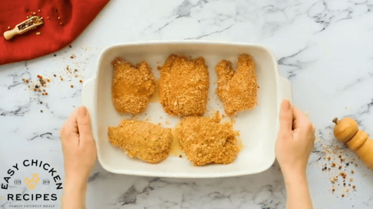 breaded chicken thighs in a baking dish topped with melted butter.