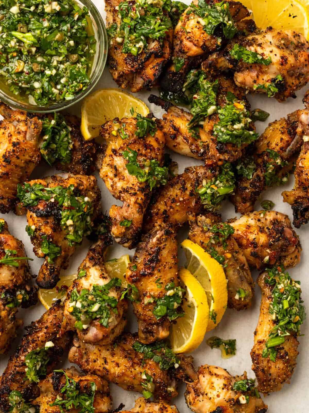 overhead view of lemon pepper wings with gremolata and lemon wedges.