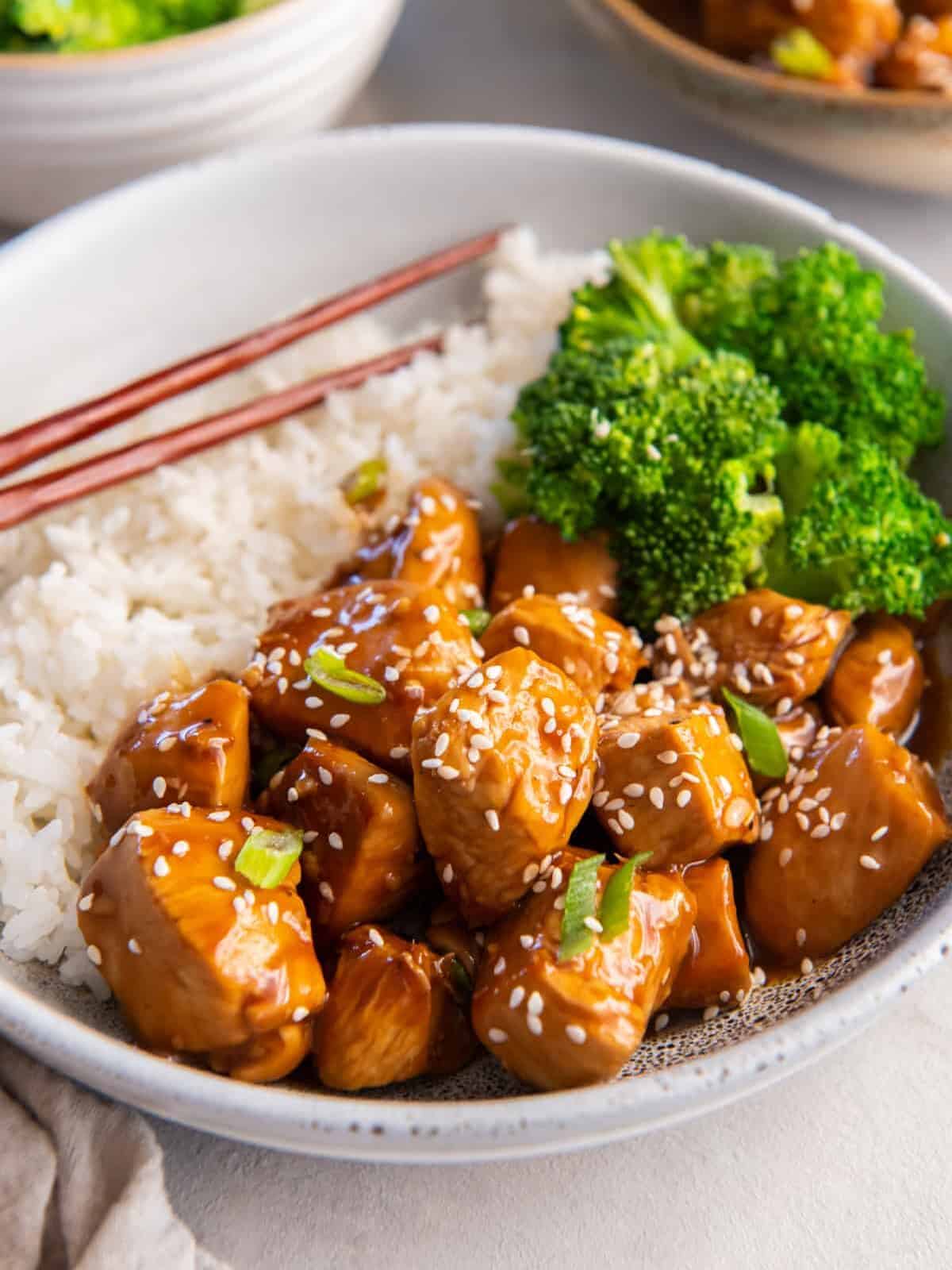 three-quarters view of mandarin chicken in a gray bowl with rice, broccoli, and chopsticks.