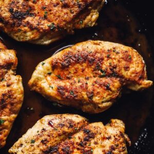 chicken breasts searing in a cast iron skillet