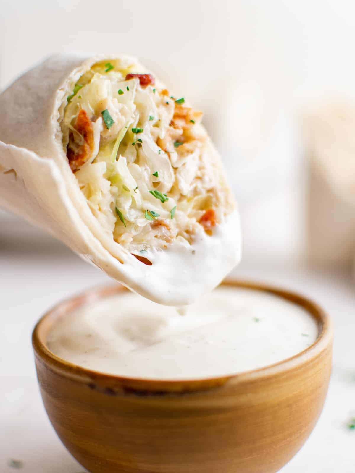 dipping a chicken ranch wrap into ranch dressing in a brown bowl