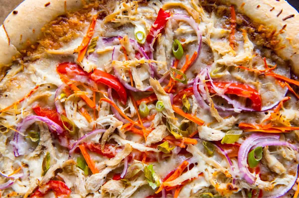 cropped overhead view of a thai chicken pizza before cutting.