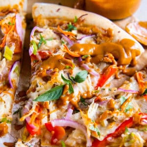 closeup of a slice of thai chicken pizza drizzled with thai peanut sauce.