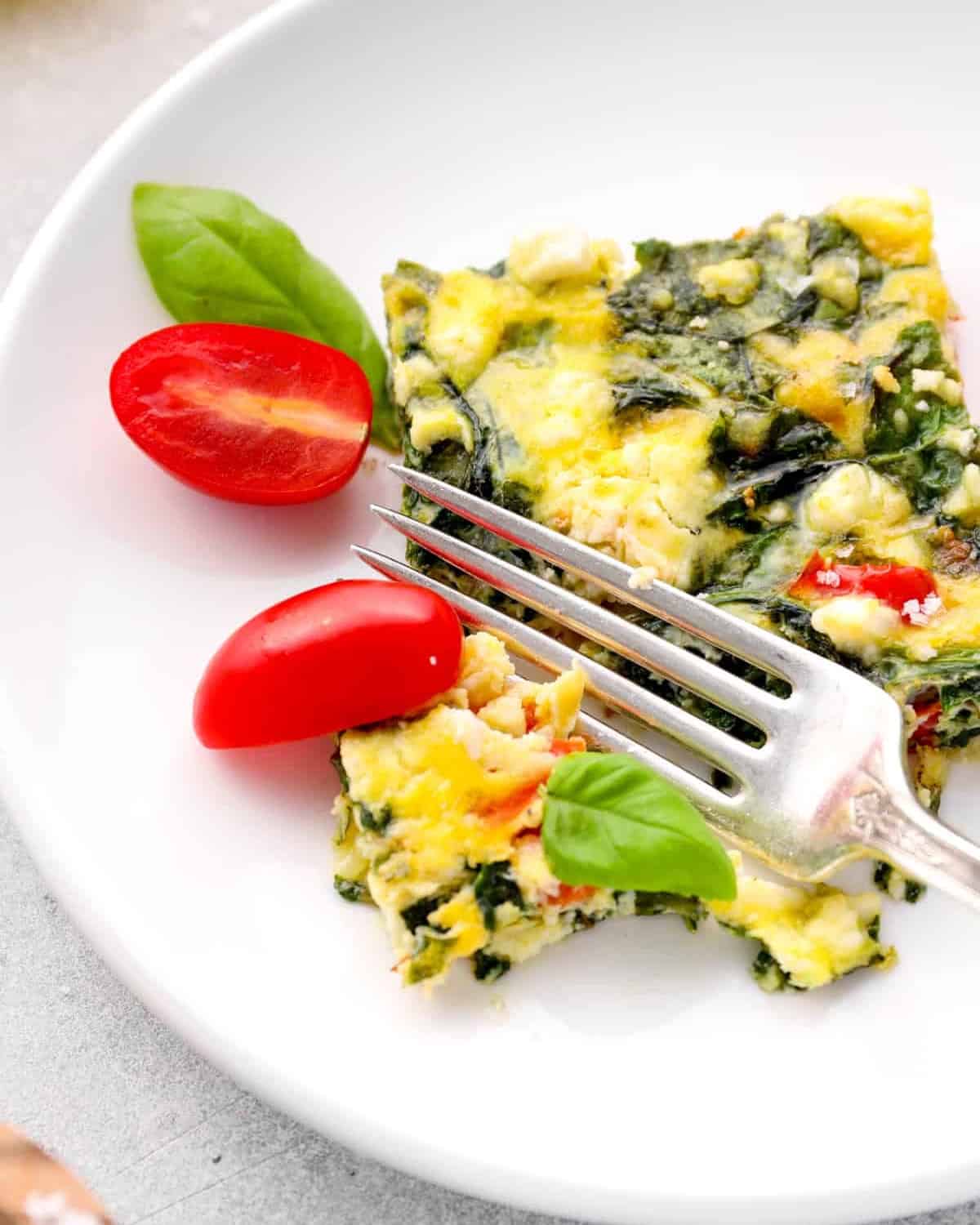 cutting a slice of vegetable frittata with a fork on a white plate.