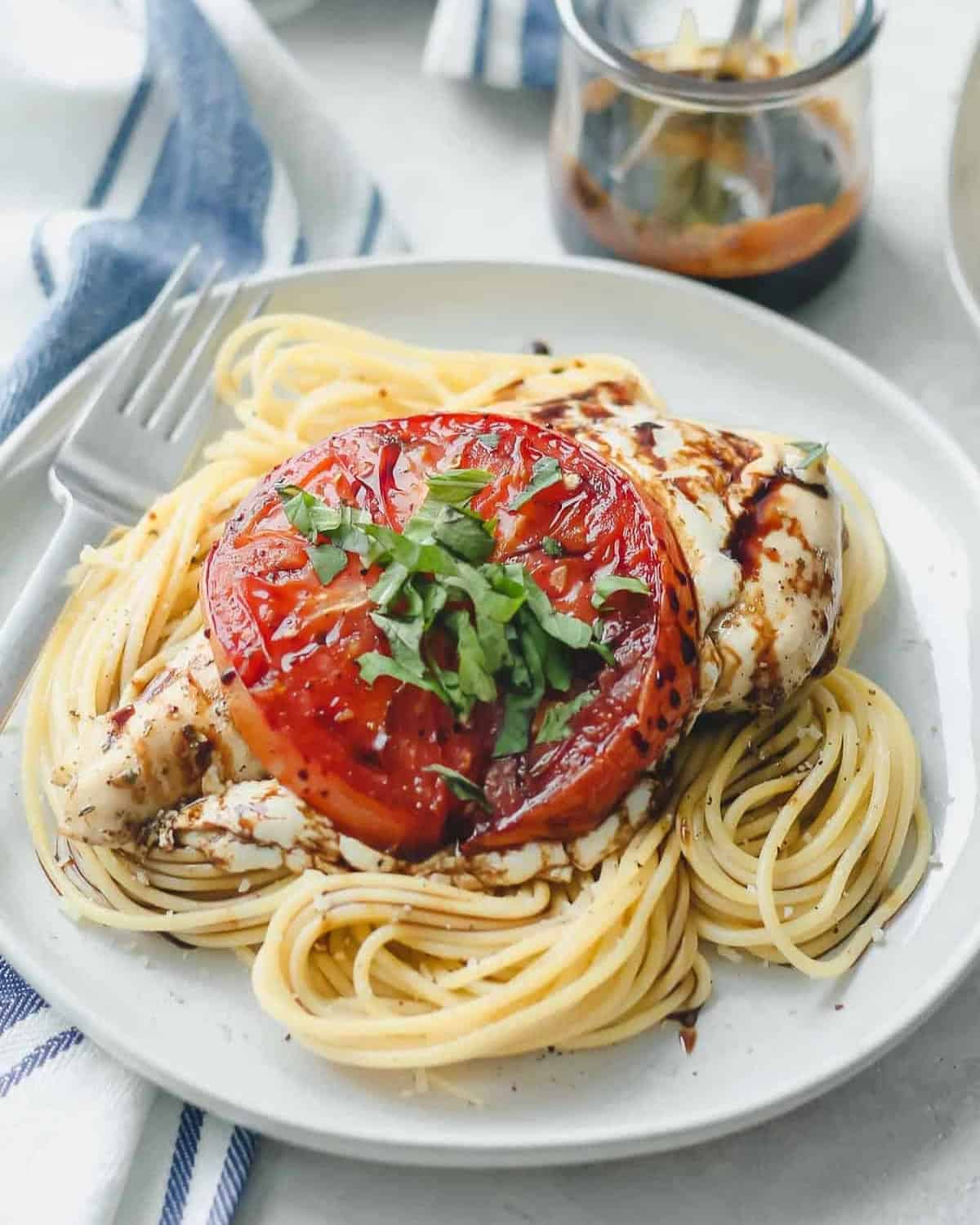 a baked caprese chicken breast on a bed of pasta.