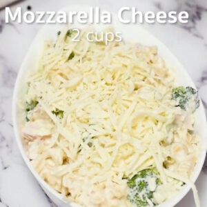 shredded mozzarella cheese over broccoli chicken alfredo in a baking dish overlaid with text "mozzarella cheese 2 cups".