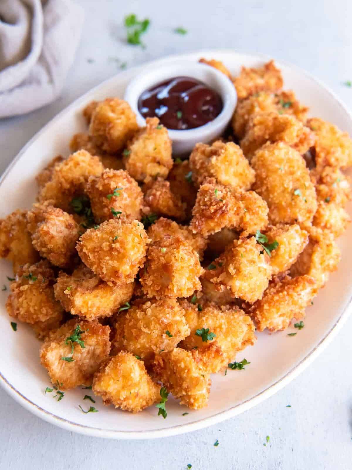 popcorn chicken on a white platter with dipping sauce.