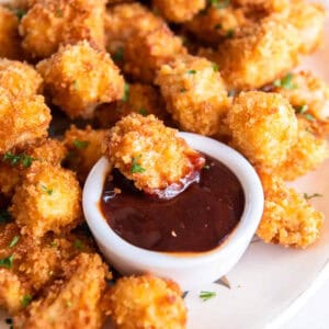 a popcorn chicken nugget dipped in bbq sauce on a platter of popcorn chicken pieces.