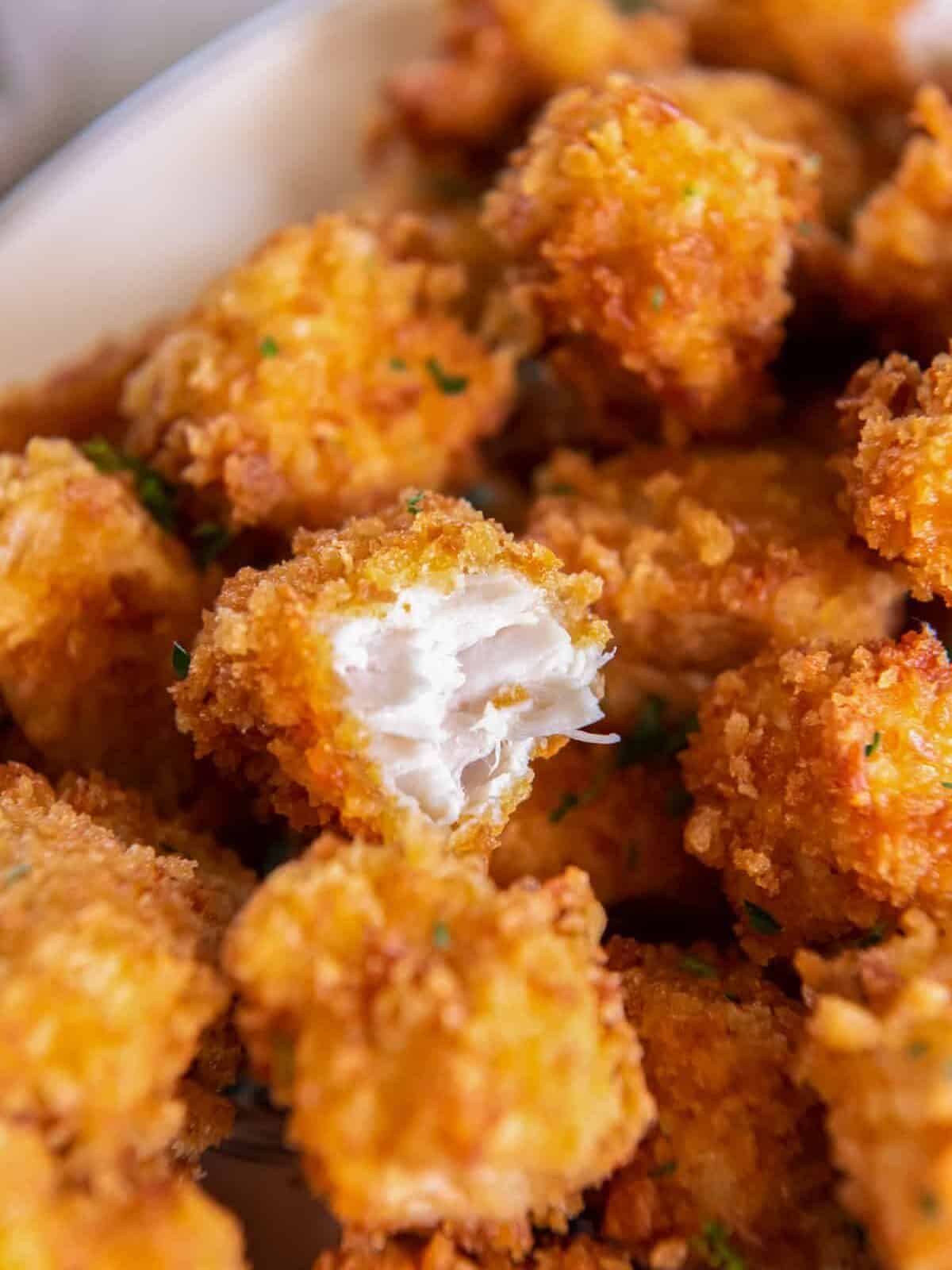 close up of a bitten piece of popcorn chicken on a pile of popcorn chicken.