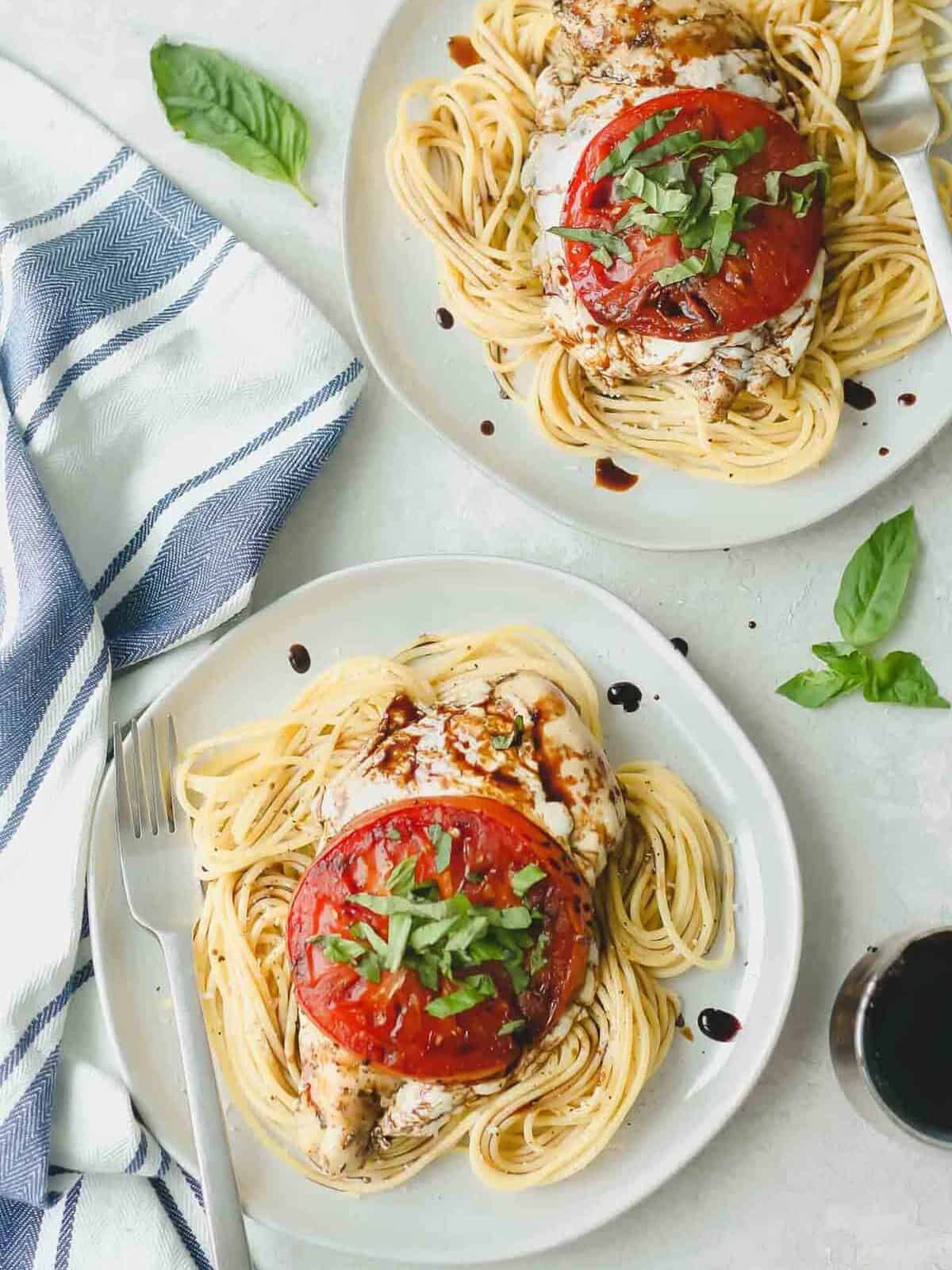 caprese chicken breasts on beds of spaghetti, plated on white dinner plates with forks