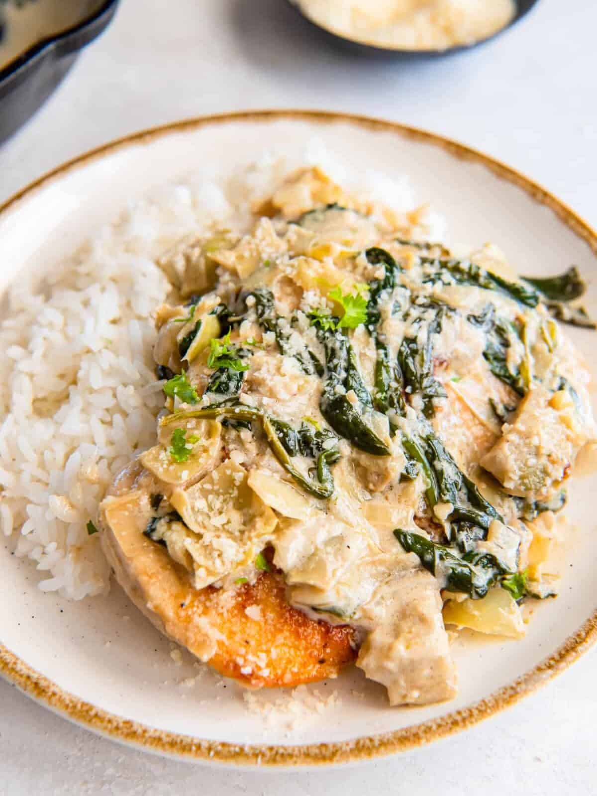 spinach artichoke chicken on a bed of white rice on a white plate.