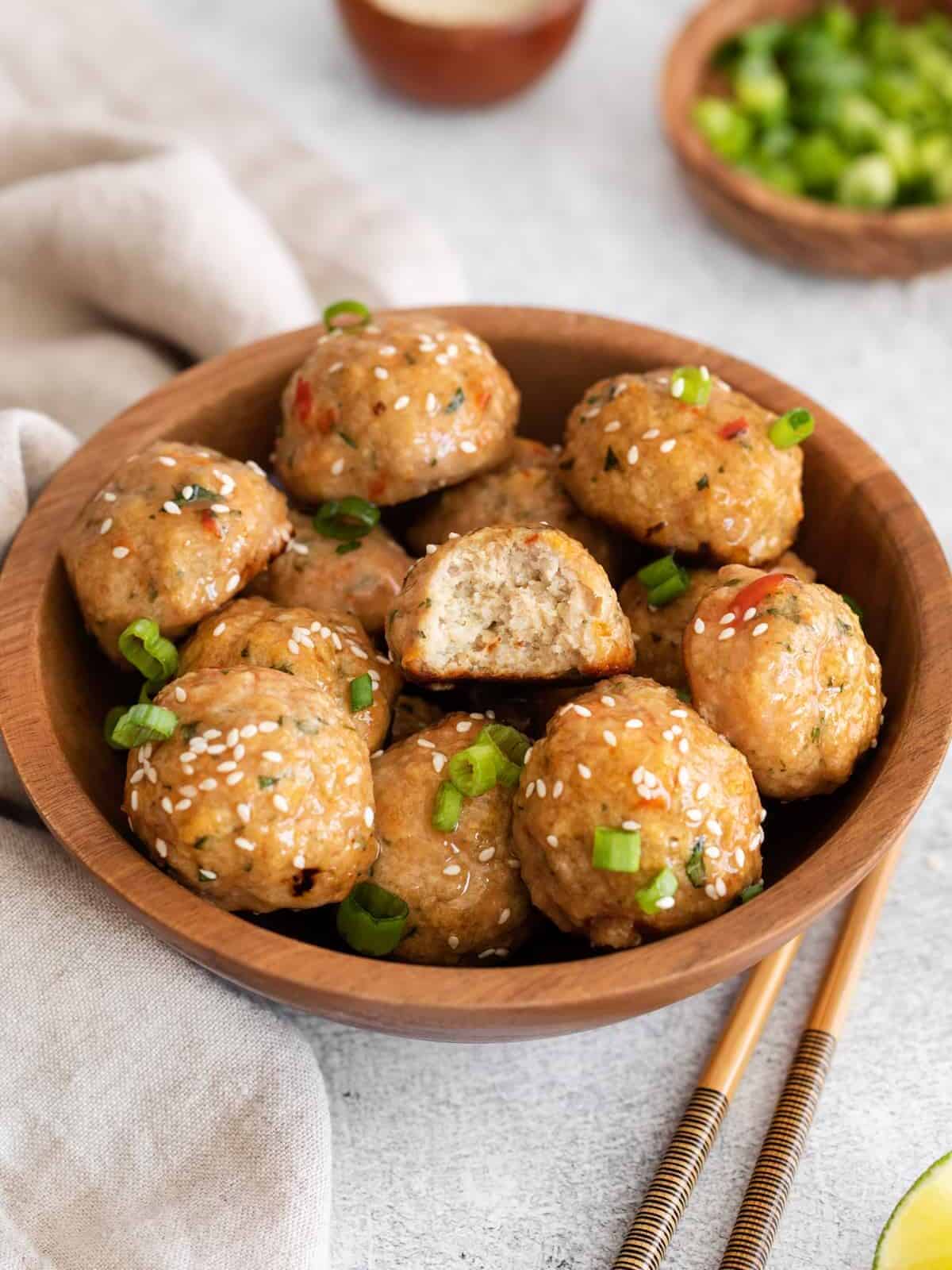 a bowl of chicken meatballs covered in sweet chili sauce, one has a bite taken out of it