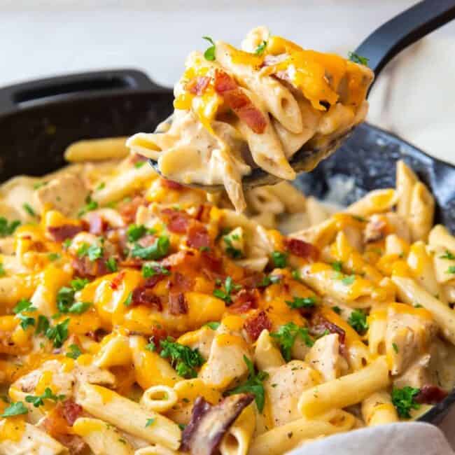 hand using a serving spoon to scoop out crack chicken pasta from a skillet