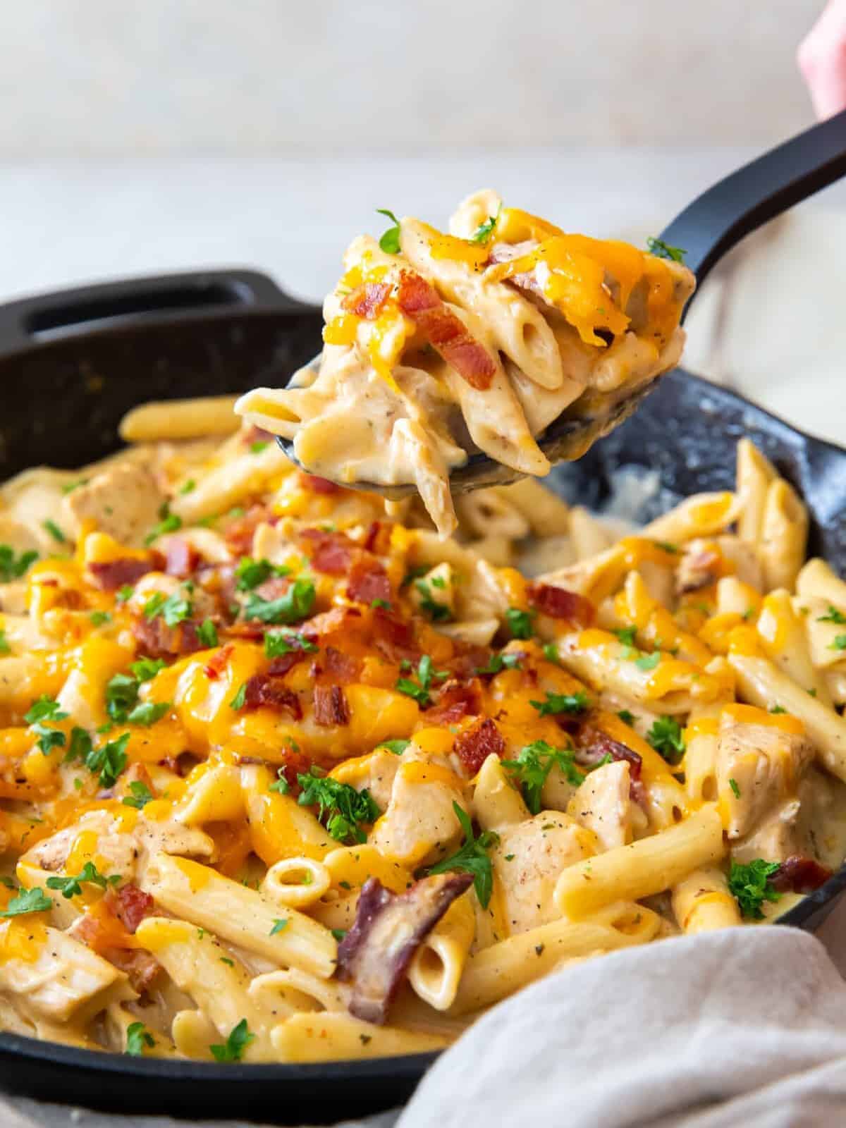 hand using a serving spoon to scoop out crack chicken pasta from a skillet