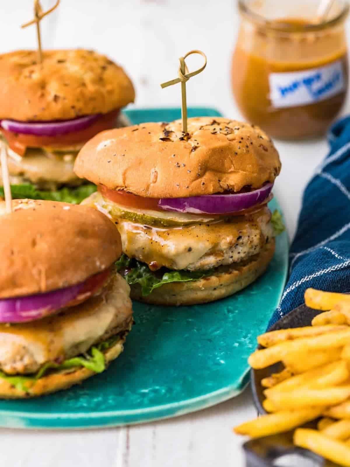ground chicken burgers on a plate, set on a table top with burger sauce and French fries set off to the side