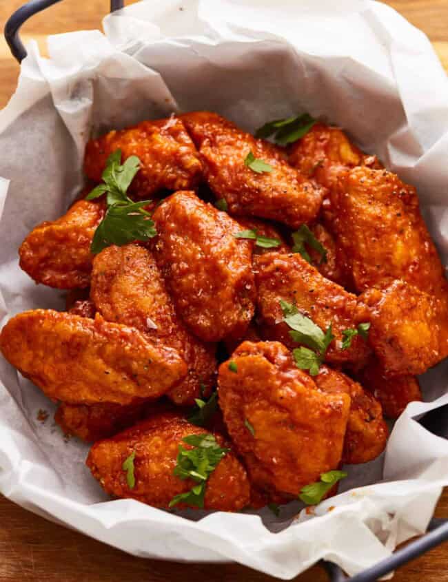 Chicken wings in a paper basket on a wooden table.