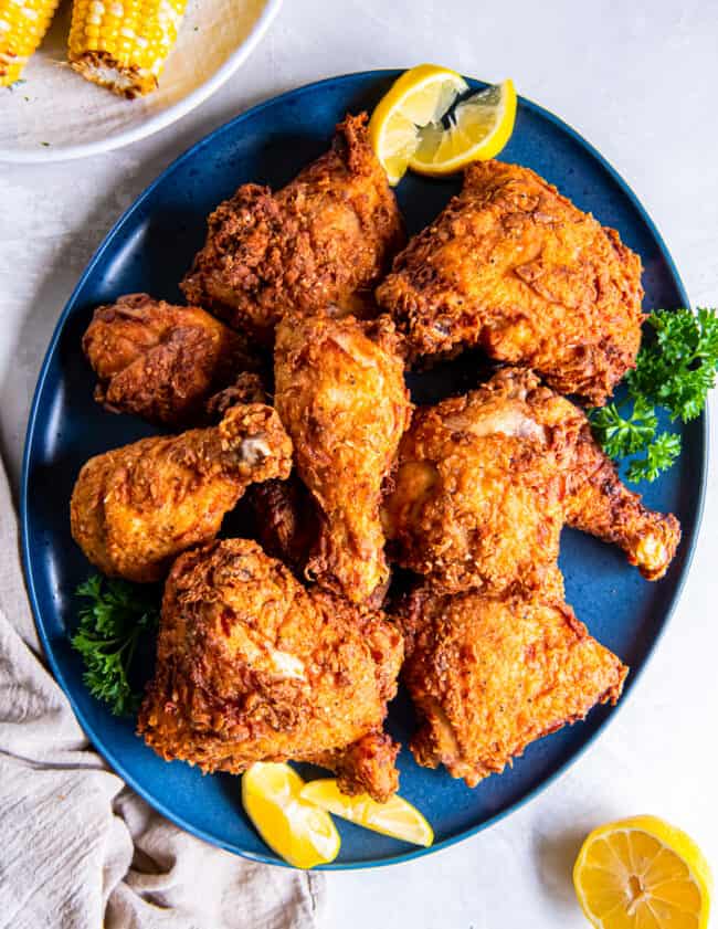 Fried chicken on a blue plate with lemons and corn on the cob.