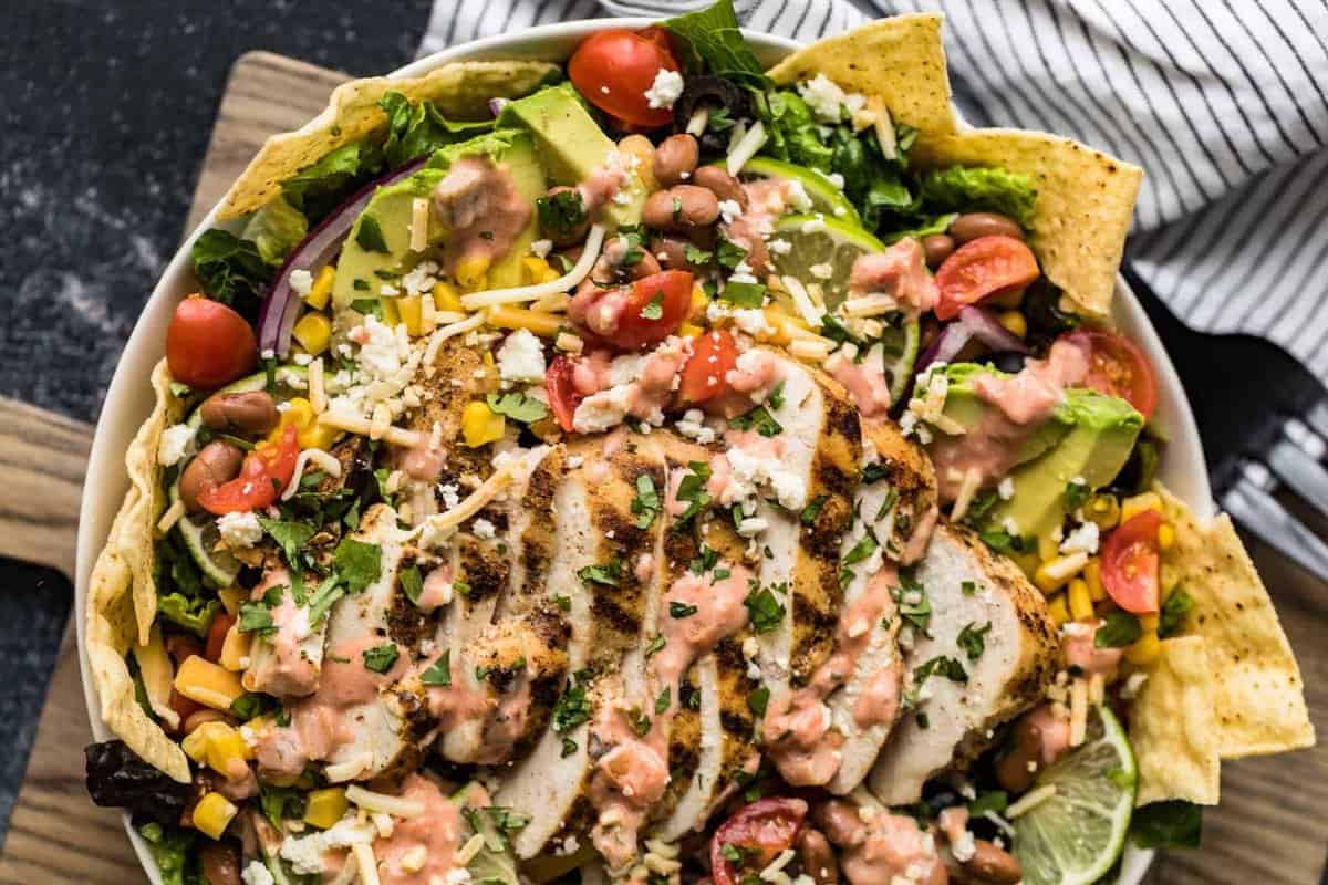 close overhead view of a large taco salad filled with grilled chicken, beans, avocado, corn, lettuce, and more