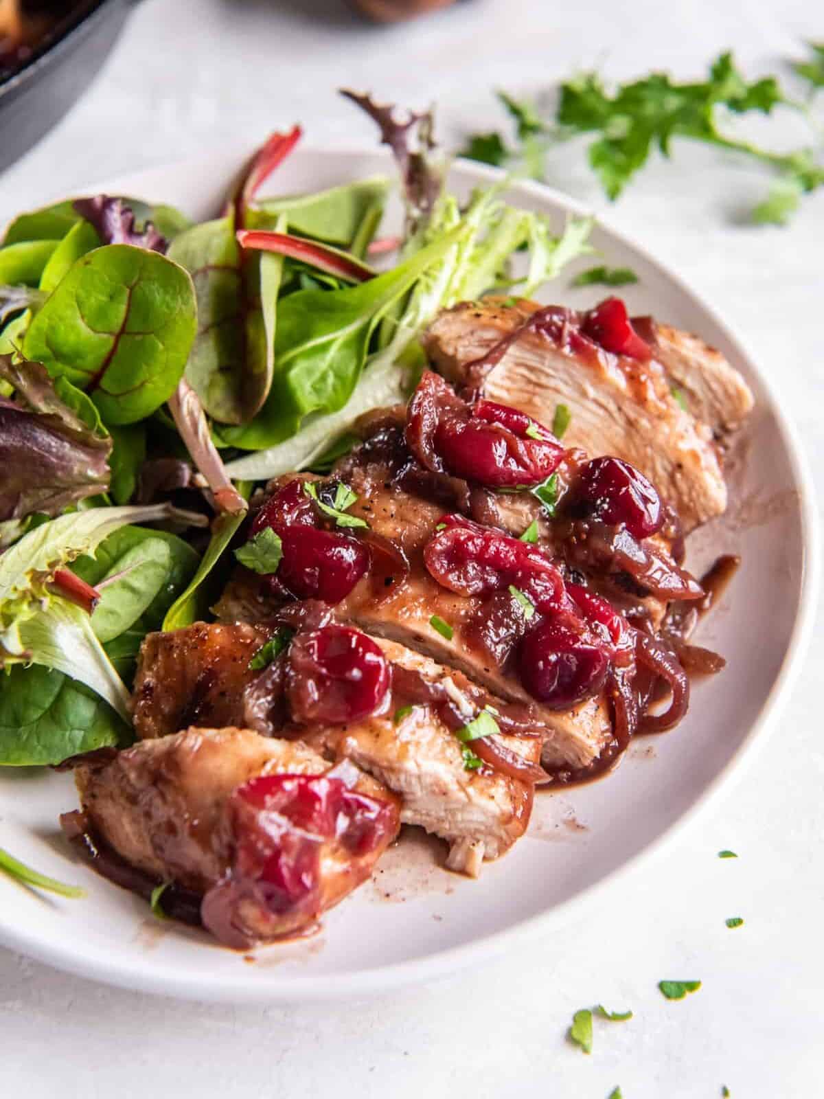 three-quarters view of a sliced cranberry chicken breast on a white plate with salad.
