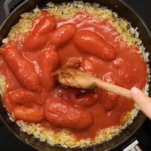 whole peeled tomatoes stirred into sautéed garlic and onions in a pan.