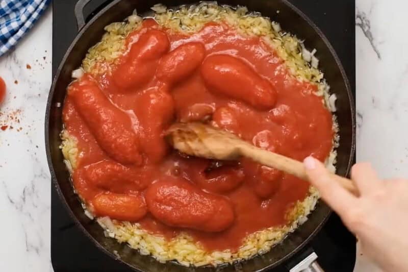 whole peeled tomatoes stirred into sautéed garlic and onions in a pan.