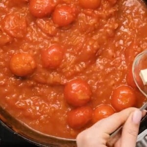 adding butter to shakshuka sauce in a pan.