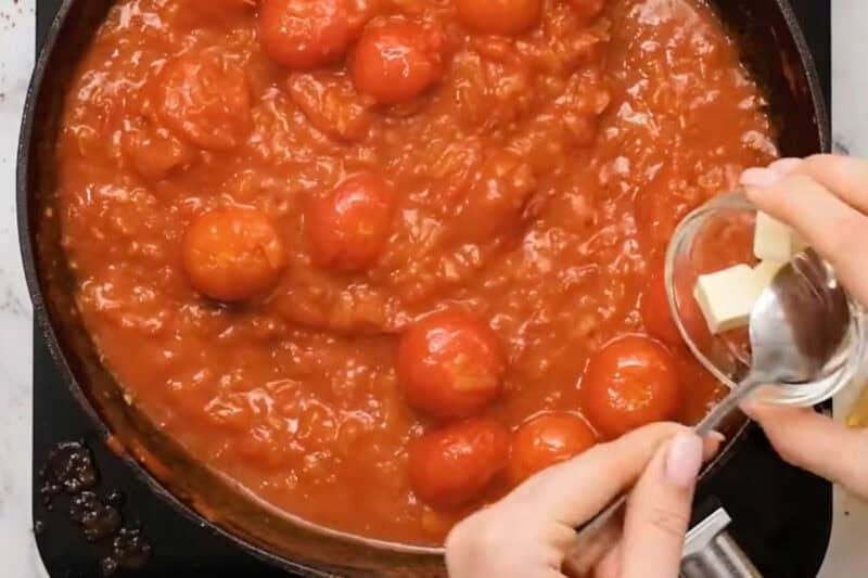 adding butter to shakshuka sauce in a pan.