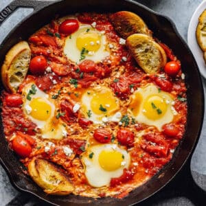 overhead view of eggs in purgatory in a cast iron skillet with slices of toasted bread.