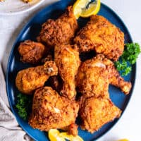 Fried chicken on a blue plate with lemon wedges.