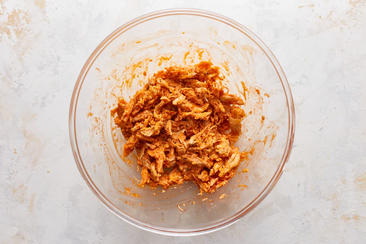 Shredded buffalo chicken in a glass mixing bowl.