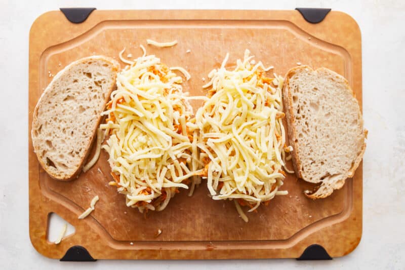 Two slices of bread with cheese on a cutting board.